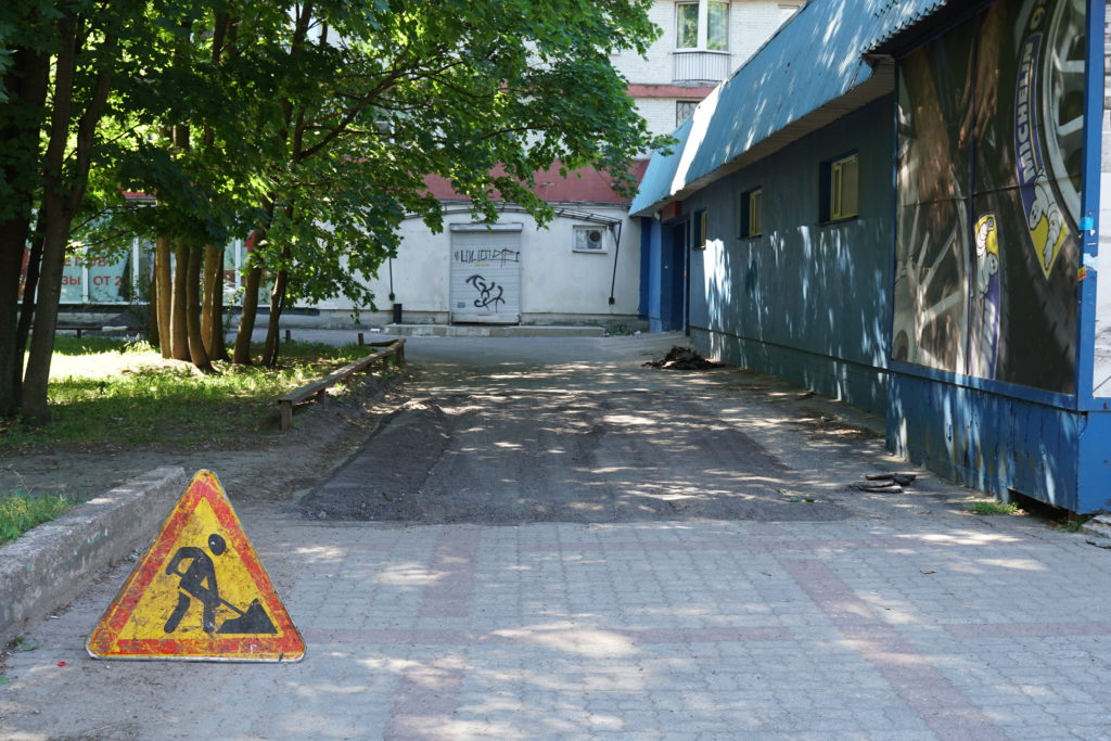 ремонтные работы по замене асфальта, знак дорожных работ, на фоне дома и зеленых деревьев