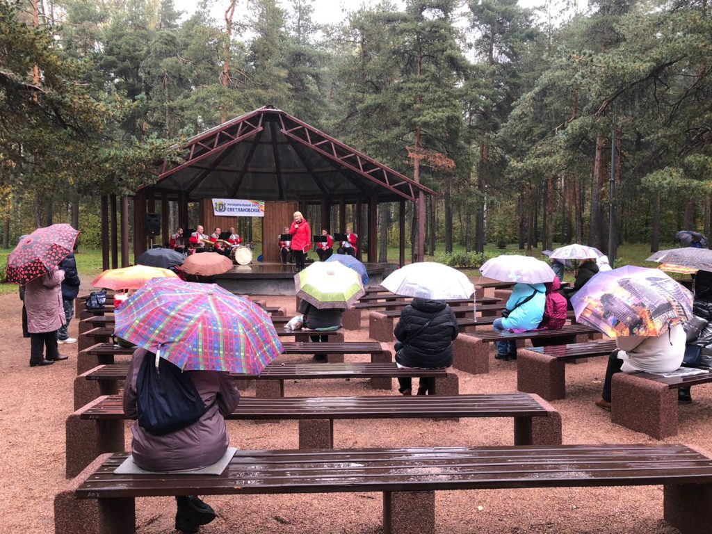 Жители МО Светлановское слушают концерт духового оркестра в парке Сосновка 25.09.2021. У всех в руках зонтики, идет дождь. 