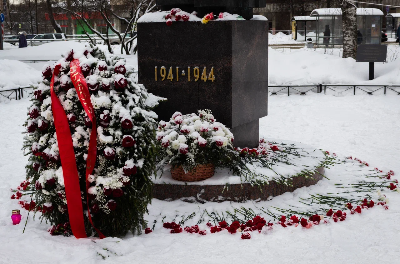 Стелла в сквере Блокадников. Рядом цветы, возложенные во время мероприятия. Вокруг снег.