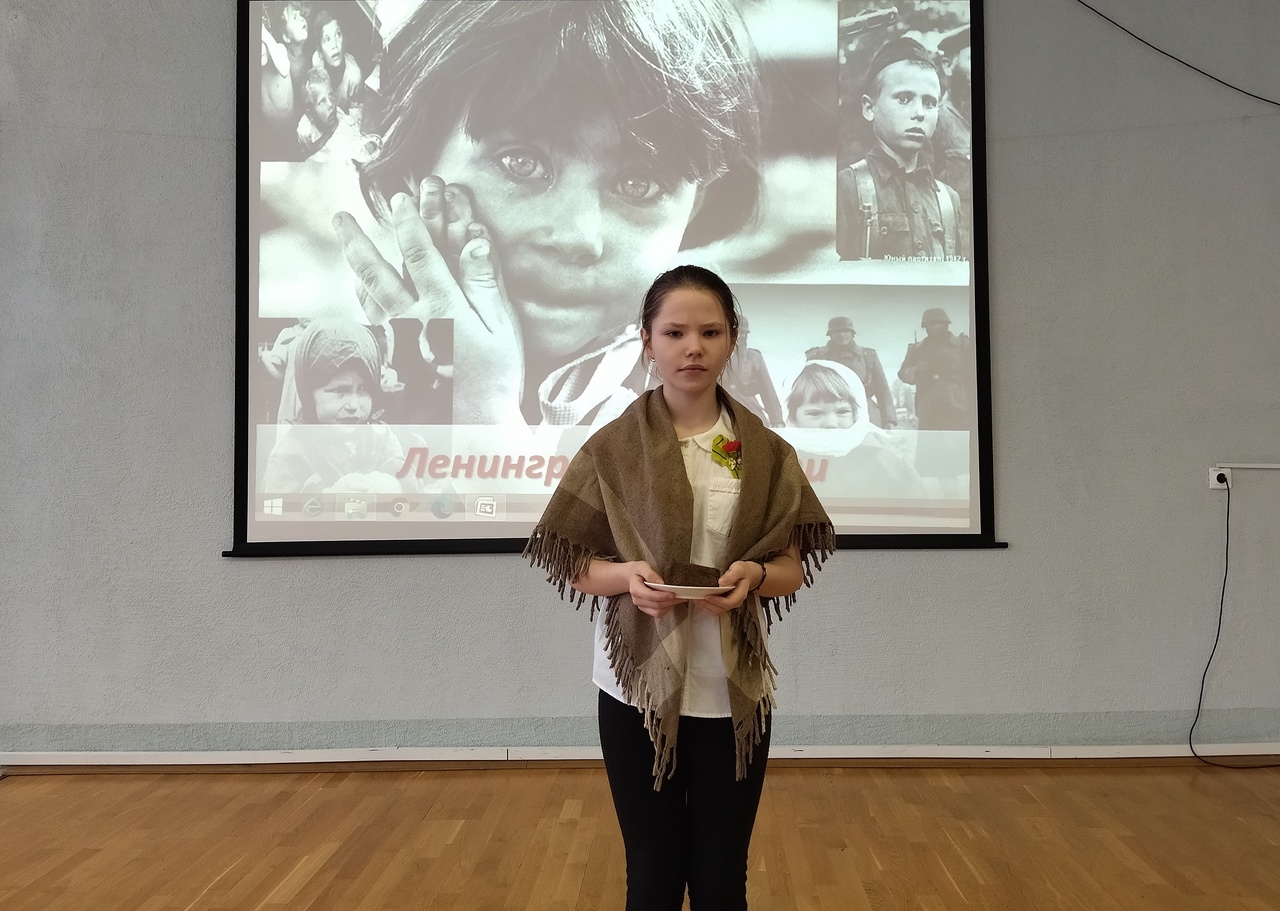 Девочка на фоне презентации с фотографиями детей времен Блокады Ленинграда во время Великой Отечественной войны 1941-1945 годов.