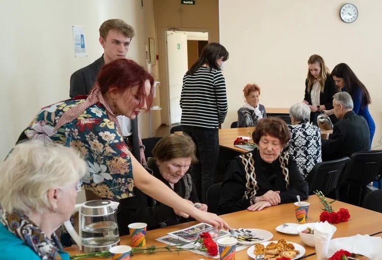 Участники Молодежного Совета МО Светлановское наливают чай для узников фашистских концлагерей, сидящих за столами. 
