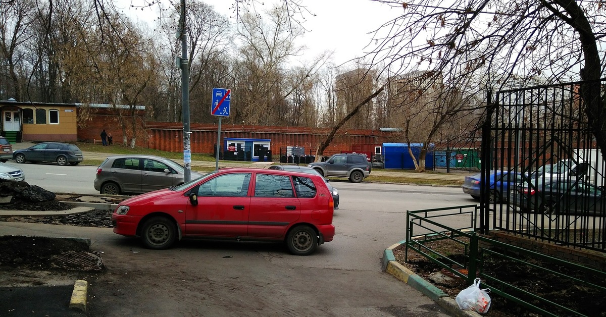 Красный автомобиль перегородил въезд во двор. НА фоне - дорога и автомобили