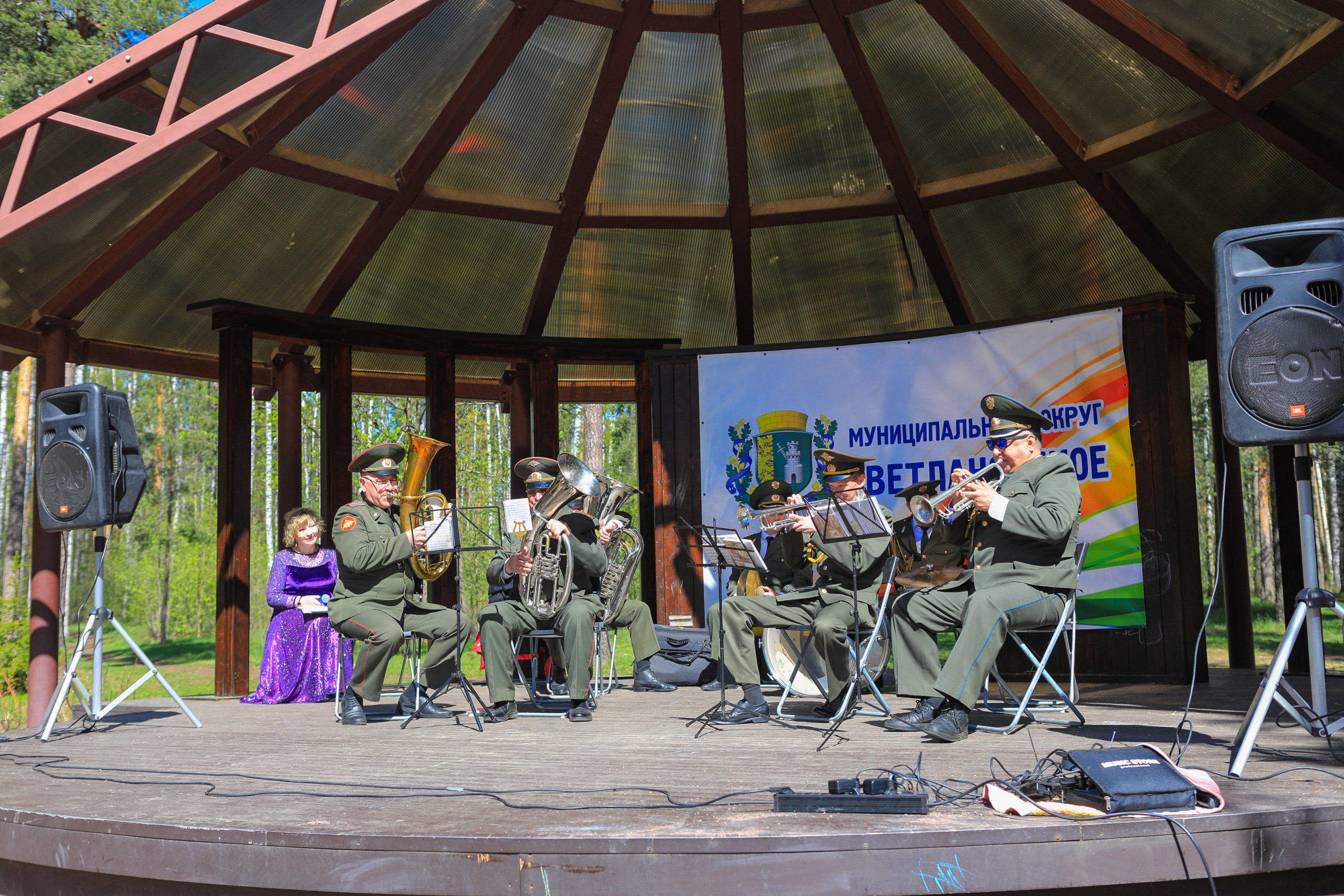 Духовой оркестр (мужчины в военной форме) играют на духовых инструментах на сцене в парке Сосновка.