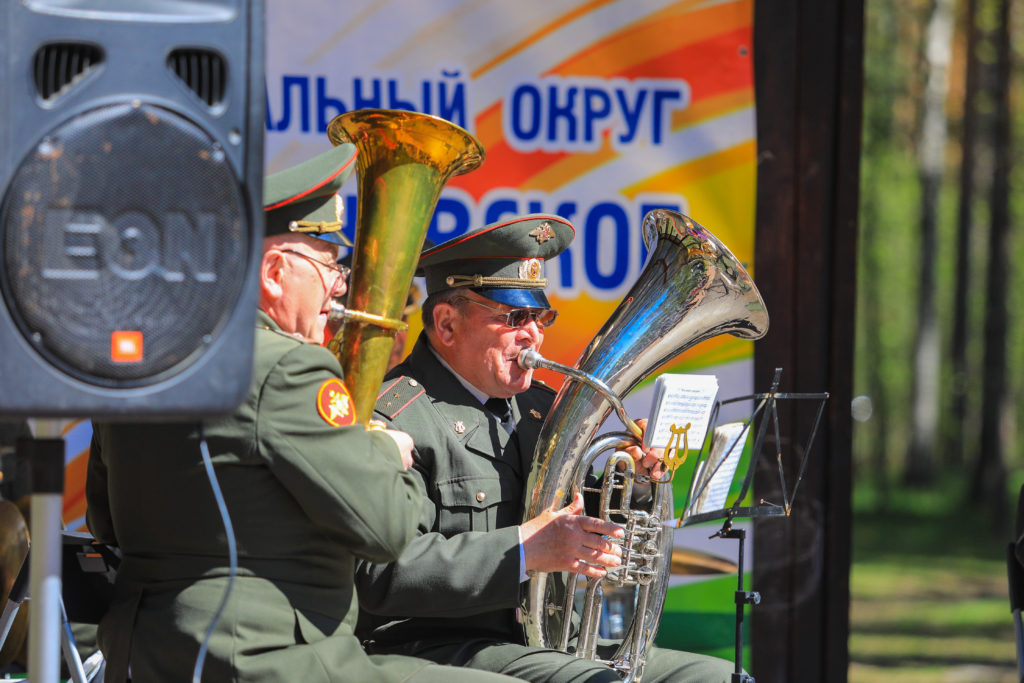 Музыканты духового оркестра (мужчины в военной форме) играют на духовых инструментах на сцене в парке Сосновка. 
