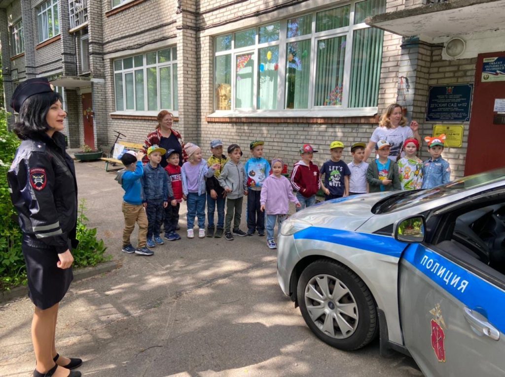 Сотрудники ГИБДД рассказывают детям о правилах дорожного движения. Дети стоят рядом с полицейским автомобилем. 
