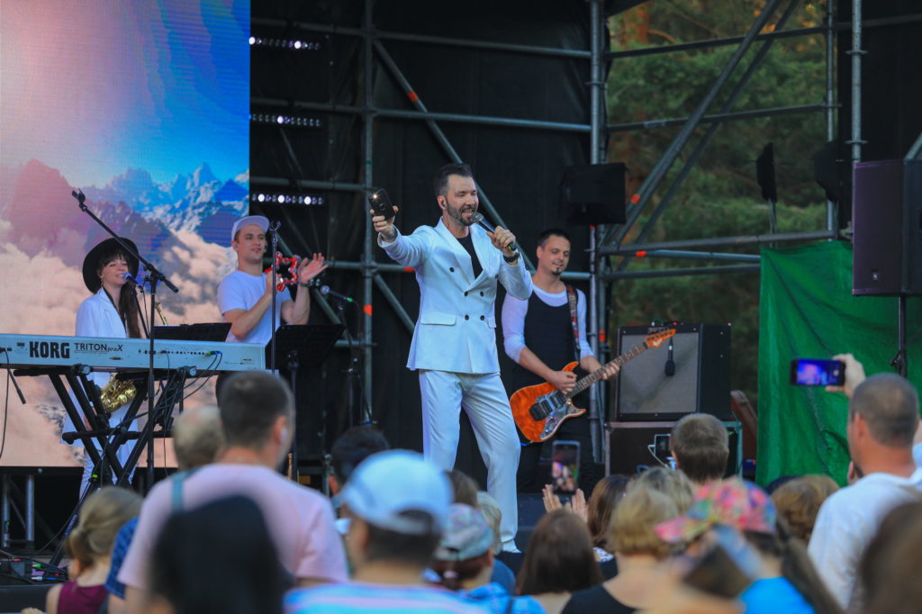 Артист Денис Клявер выступает на сцене с музыкантами. 
