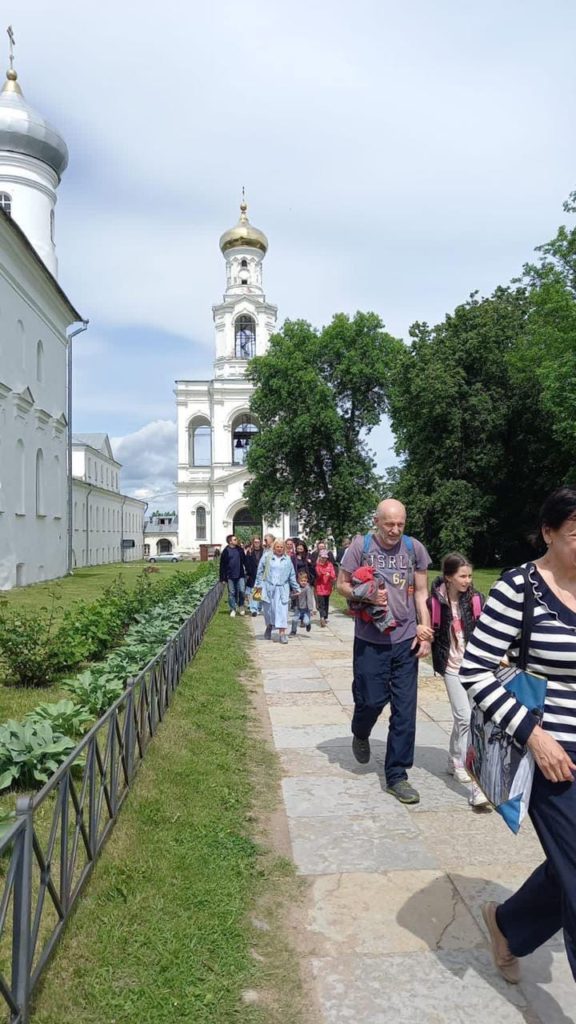 Люди на экскурсии в Великом Новгороде на фоне белокаменной церкви с золотыми куполами. 