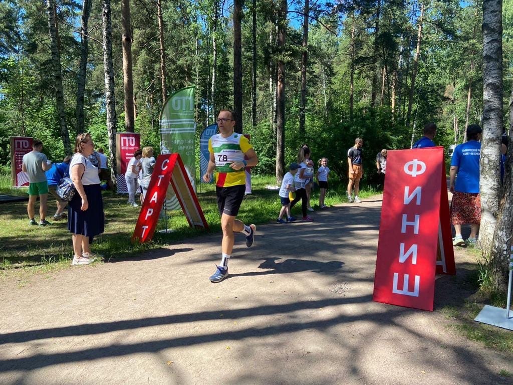 Участник забега финиширует в парке Сосновка. На фоне - зеленые лес и газоны. 