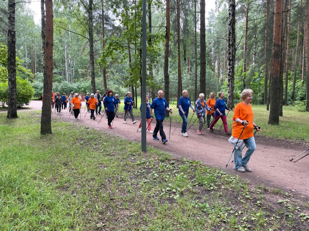 На фото: группа жителей МО Светлановское в оранжевых и синих футболках занимаются скандинавской ходьбой в парке Сосновка. 
